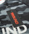 A close up view of the 9Round black tag with a red logo over the front of a black and grey camo t-shirt
