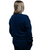 A person with blonde hair is standing with their back to the camera, wearing a navy-blue sweatshirt and pants against a white background.
