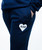 Person wearing navy blue sweatpants with a white heart-shaped patch labeled ILKB on the thigh; one hand is in the pocket.