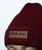 A burgundy cable knit beanie with a brown leather patch that reads 9ROUND