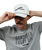 Man with a mustache adjusts a white Southpaw Kickboxer cap while wearing a gray Stronger Every Day 9Round t-shirt against a plain white background.
