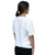 A woman with brown hair in a ponytail is standing and facing away, wearing a plain white t-shirt and black pants against a white background.