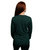 Person with long red hair wearing a dark green long-sleeve shirt and black pants, facing away from the camera against a white background.