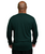 A bald man seen from behind wearing a long-sleeve dark green shirt and black pants, standing against a white background.