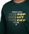 A person wears a dark green shirt with the text: Strength is built one rep, one hit, one day at a time in white and yellow letters.