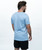 A man stands facing away from the camera, wearing a light blue t-shirt and black shorts against a plain white background.