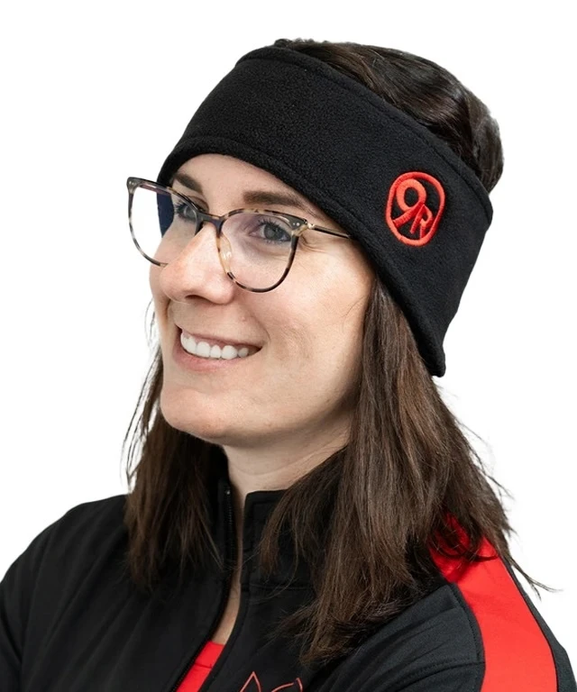 A woman with dark brown hair wearing a black fleece headband with a red embroidered 9Round circle logo.