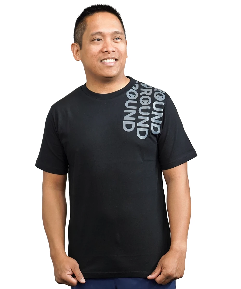 A man with short black hair wearing a black t-shirt with the 9Round logo repeated three times across the shoulder in a matte grey color for a cool street-style design.