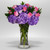 A graceful floral arrangement designed with soft hydrangeas, lavender-toned roses, and fresh greenery in a clear glass vase.