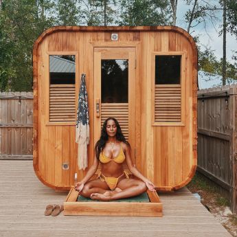 Woman performing yoga in front of Redwood Outdoors cube sauna