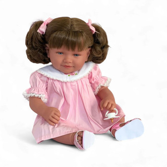 Ann Lauren Dolls Baby Dimples brunette toddler doll with brown hair in pigtails, blue eyes, pink smocked dress, white sandals, and pacifier.