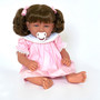 Ann Lauren Dolls Baby Dimples brunette toddler doll with brown hair in pigtails, blue eyes, pink smocked dress, white sandals, and pacifier.