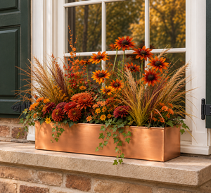 Real Copper Liner or window box with autumnal flowers on a ledge with a home with shutters.