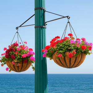 Two Way Hanging Basket Bracket on green post holding 2 hanging baskets filled with flowers with ocean in background Two Way Hanging Basket Bracket on green post holding 2 hanging baskets filled with flowers with ocean in background