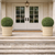 2 French Basket Round GFRC Planters with green round hedges in natural finish flanking a front door w