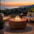 Zaragoza round fire table shown in oxido on a deck with sea side community in background