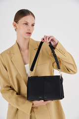 Profile view of model wearing the Oroton Emma Small Day Bag in Black and Pebble Leather for Women .
