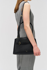 Profile view of model wearing the Oroton Audrey Small Three Pocket Day Bag in Black and Premiums saffiano and smooth leather for Women .