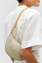 Profile view of model wearing the Oroton Isla Short Chain Strap in Brass and Brass for Women .
