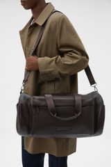 Profile view of model wearing the Oroton Ethan Pebble Weekender in Bitter Chocolate and Pebble Leather for Men .