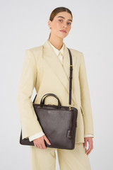 Profile view of model wearing the Oroton Muse Apple 15" Slim Laptop Bag in Dark Chocolate and Vegan leather for Women