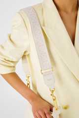Profile view of model wearing the Oroton Logo Webbing Bag Strap in Clotted Cream and Smooth leather for Women .