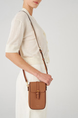 Profile view of model wearing the Oroton Dylan Buckle Phone Crossbody in Tan and Pebble leather, smooth leather trims for Women