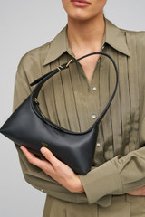 Profile view of model wearing the Oroton Cinder Mini Baguette in Black and Smooth leather for Women .
