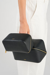 Profile view of model wearing the Oroton Fife Medium Beauty Case in Black and Pebble leather for Women .