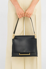 Profile view of model wearing the Oroton Elm Medium Satchel in Black and Premium smooth pebble leather for Women .