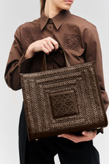 Profile view of model wearing the Oroton Lane Straw Medium Tote in Mahogany and Woven straw with leather trims for Women