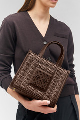Profile view of model wearing the Oroton Lane Straw Small Tote in Mahogany and Woven straw with leather trims for Women