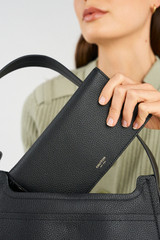 Profile view of model wearing the Oroton Eve Soft Fold Wallet in Black and Pebble leather exterior for Women .
