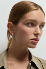 Profile view of model wearing the Oroton Ribbon Twist Huggies in Gold and Brass with sterling silver earring post for Women .