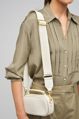 Profile view of model wearing the Oroton Logo Bag Strap in Clotted Cream and Premium leather and webbing material for Women .