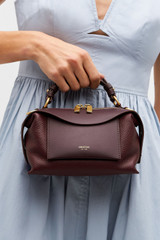 Profile view of model wearing the Oroton Mica Mini Bowler in Currant and Premium pebble leather for Women .