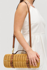 Profile view of model wearing the Oroton Billie Wicker Wine Holder in Brandy and Wicker exterior with leather trims for Women .