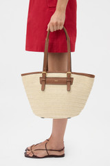 Profile view of model wearing the Oroton Camille Straw Medium Tote in Natural and Woven straw with leather trims exterior for Women .