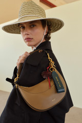 Profile view of model wearing the Oroton Zig Zag Keyring in ANISEED and Premium crackle leather for Women .
