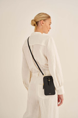 Profile view of model wearing the Oroton Dylan Phone Crossbody in Black and Premium pebble leather for Women .