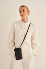 Profile view of model wearing the Oroton Dylan Phone Crossbody in Black and Premium pebble leather for Women .