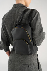 Profile view of model wearing the Oroton Dylan Small Backpack in Black and Pebble leather for Women .