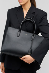 Profile view of model wearing the Oroton Muse 15" Worker Tote in Black and Saffiano leather exterior for Women .