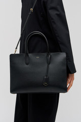 Profile view of model wearing the Oroton Muse 15" Worker Tote in Black and Saffiano leather exterior for Women .