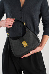 Profile view of model wearing the Oroton Yvonne Signature Baguette in Black and Nylon canvas base cloth material with PVC coating (70% PVC, 30% polyester) for Women .