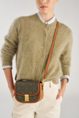 Profile view of model wearing the Oroton Yvonne Signature Small Saddle Bag in Cognac and Nylon canvas base cloth material with PVC coating (70% PVC, 30% polyester) for Women .