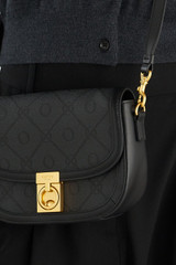 Profile view of model wearing the Oroton Yvonne Signature Small Saddle Bag in Black and Nylon canvas base cloth material with PVC coating (70% PVC, 30% polyester) for Women .