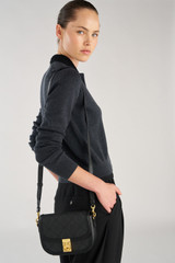 Profile view of model wearing the Oroton Yvonne Signature Small Saddle Bag in Black and Nylon canvas base cloth material with PVC coating (70% PVC, 30% polyester) for Women .