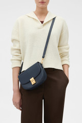 Profile view of model wearing the Oroton Yvonne Small Saddle Bag in DARK NAVY and Premium pebble leather for Women .
