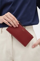 Profile view of model wearing the Oroton Eve Slim Zip Wallet in BERRY and Premium pebble leather for Women .